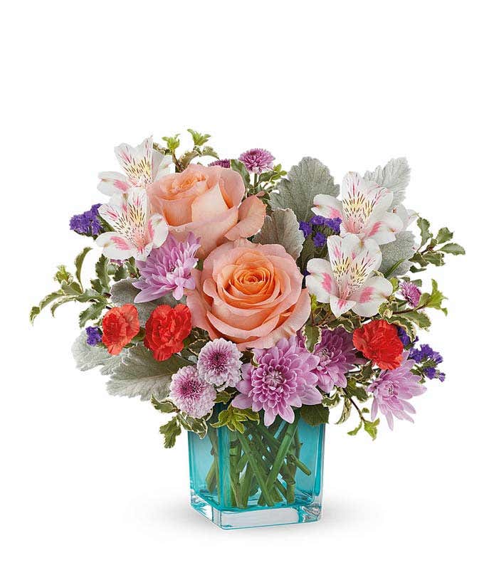 A bouquet featuring peach roses, pink alstroemeria, miniature orange carnations, and lavender cushion spray chrysanthemums in a blue glass vase.