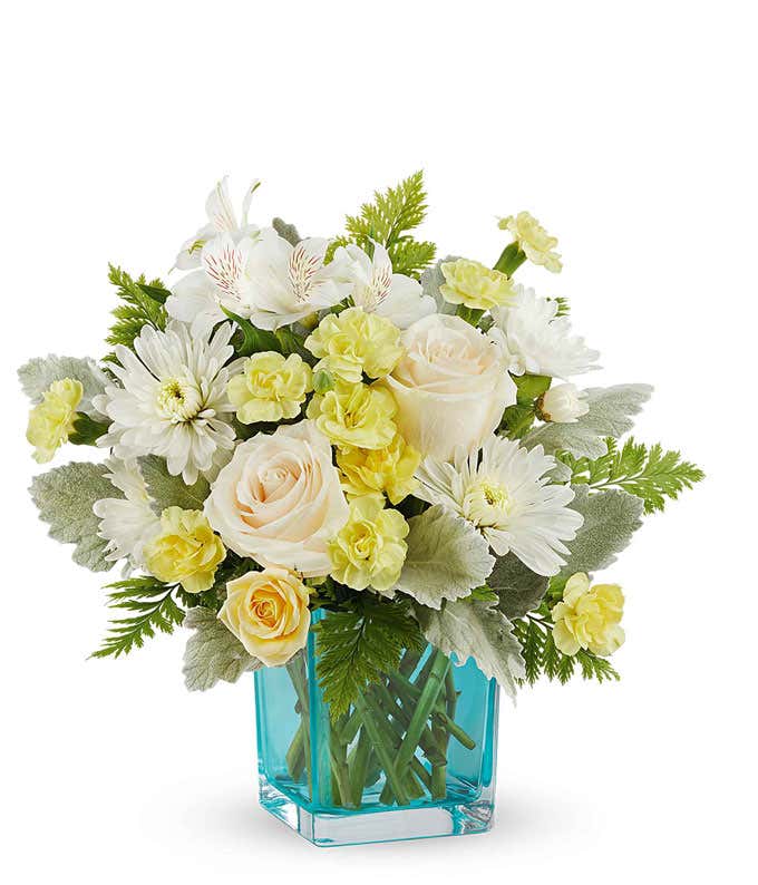 Cheerful floral arrangement with creamy white roses, soft yellow spray roses, white alstroemeria, white mums, and yellow carnations in a vibrant blue glass vase, perfect gift for loved ones.