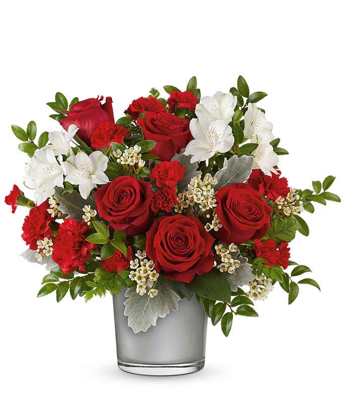 Red roses with white alstroemeria, red carnations, delicate white accents, and greenery arranged in a modern silver glass vase