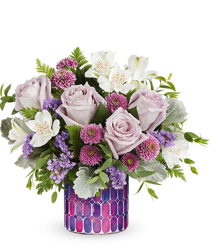 Lavender Roses, White Alstroemeria, Lavender Button poms, and floral greenery in a purple mosaic Cylinder Container