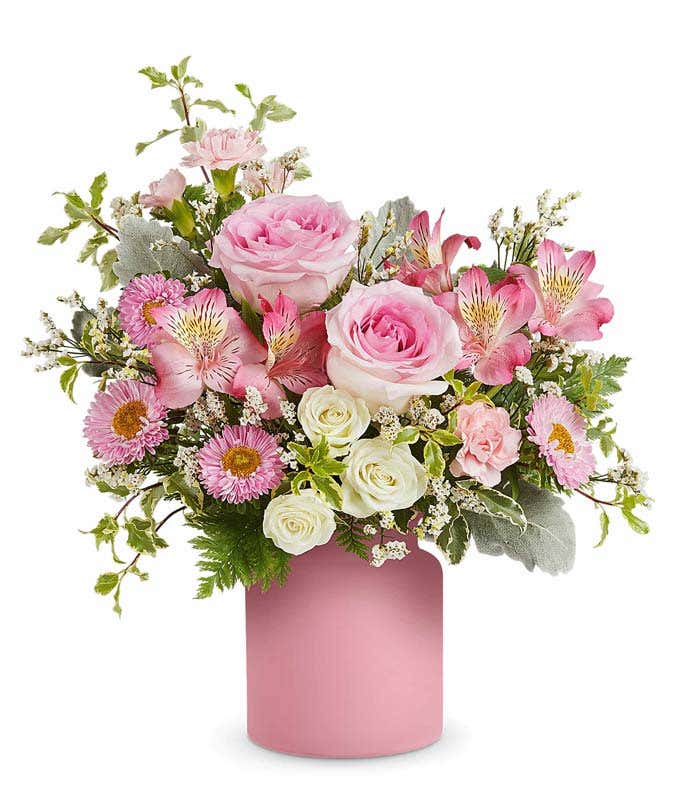 Pink roses, white sprat roses, pink alstroemeria, mini carnations and asters, and floral greenery in an opaque pink Savannah Jar