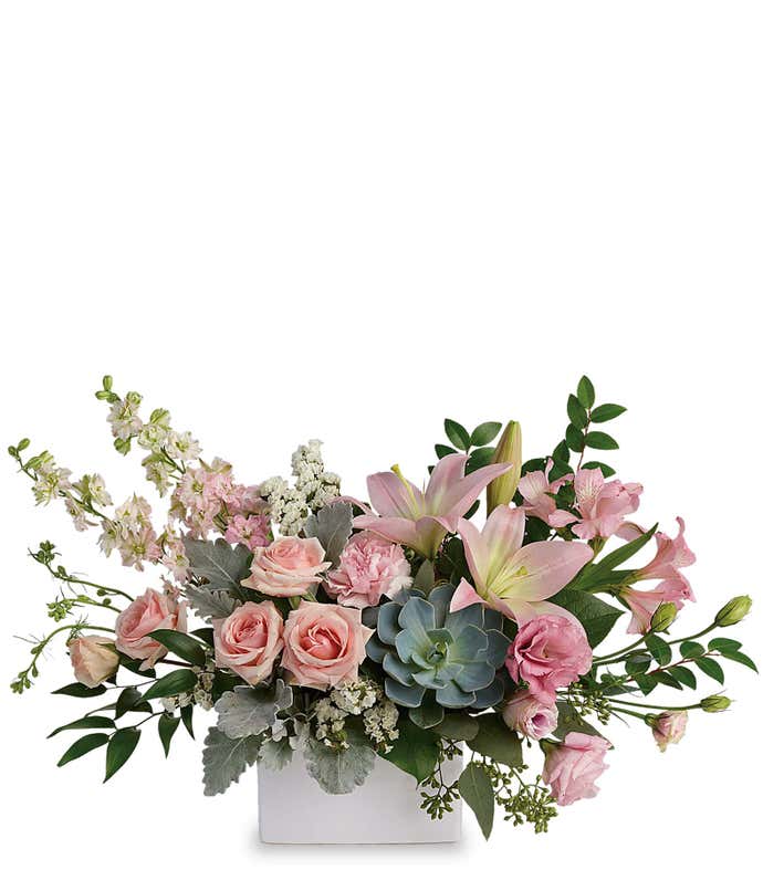 A beautiful arrangement featuring pink spray roses, pink lilies, pink alstroemeria, pink carnations, pink lisianthus, pink larkspur, white statice, and an echeveria succulent, all presented in a keepsake vase. This vibrant pink display offers a charming a
