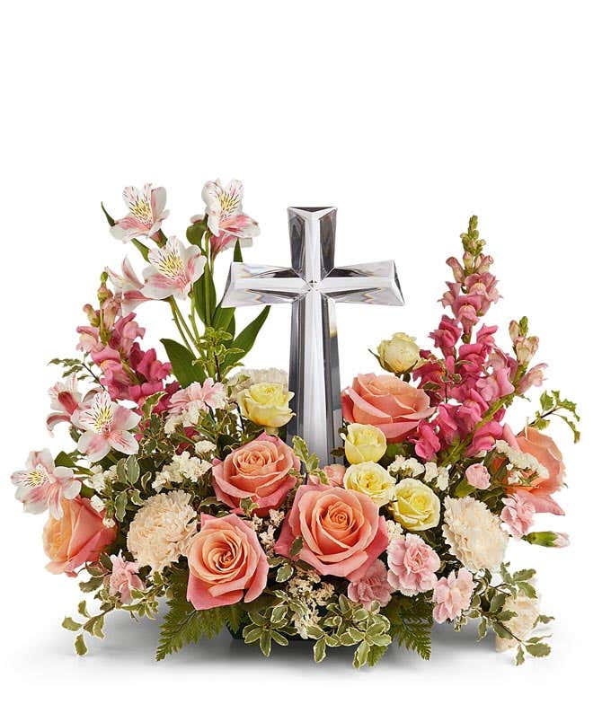 Coral roses, yellow spray roses, pink alstroemeria, creme carnations, mini pink carnations, hot pink snapdragons, and floral greenery with a large crystal cross on top of the arrangement