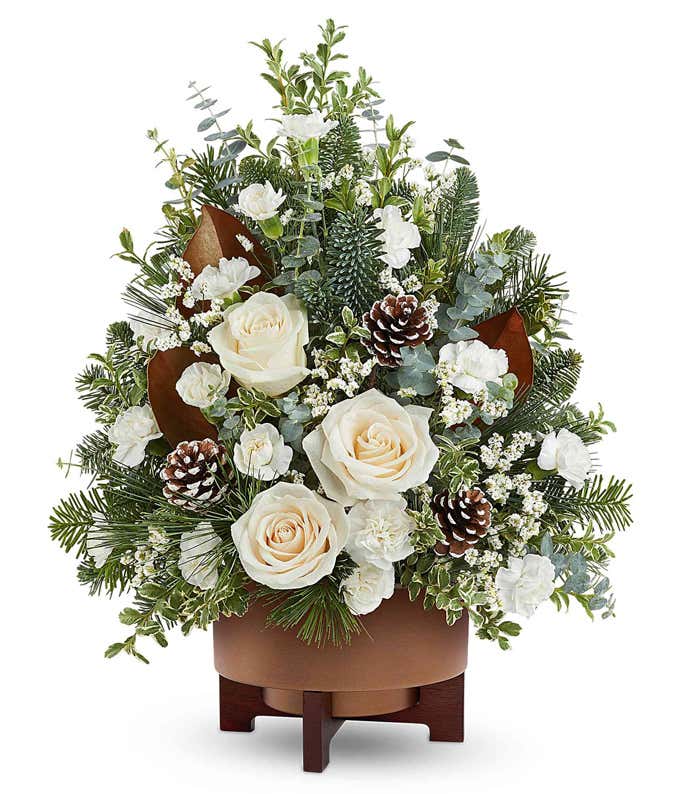 Christmas tree-shaped floral arrangement with white roses, white carnations, white limonium, frosted pinecones, seasonal greenery, and eucalyptus in a brown ceramic container.