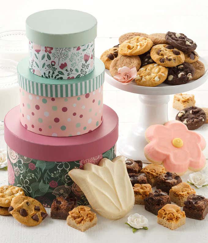 An elegant tower of Mother's Day treats, including Nibblers Bite-Sized Cookies, Brownie Bites, and Frosted Cookiesa Daisy and a Tulip. Adorned with floral designs, it's a sweet and thoughtful way to celebrate Mom's special day.