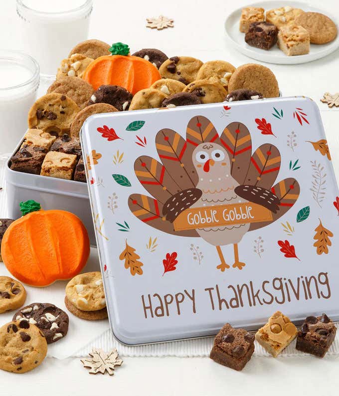 Cookie tin with turkey illustration, inside are assorted flavors of bite-sized cookies and brownie bites. One cookie is frosted to look like a pumpkin, another like a leaf.