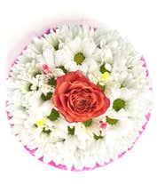 Alternative image 1 for A floral arrangement designed to resemble a birthday cake, featuring layers of white daisies, green button mums, and pink carnations. The top layer is accented with a single peach rose and three striped candles, with a decorative pink lace trim around the