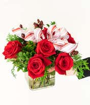 Alternative image 1 for A festive arrangement with red roses, white carnations, red hypericum berries, displayed in a glass cube vase with a decorative ribbon.