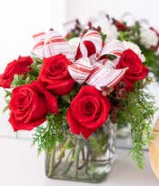 Alternative image 2 for A festive arrangement with red roses, white carnations, red hypericum berries, displayed in a glass cube vase with a decorative ribbon.