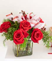 Alternative image 3 for A festive arrangement with red roses, white carnations, red hypericum berries, displayed in a glass cube vase with a decorative ribbon.