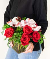 Alternative image 4 for A festive arrangement with red roses, white carnations, red hypericum berries, displayed in a glass cube vase with a decorative ribbon.