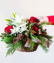 Alternative image 4 for A brown woven basket filled with white lilies, red carnations, red roses, white poms, red berries, and christmas greens with a handle. 