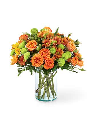 A vibrant floral arrangement featuring orange roses, orange spray roses, butterscotch daisies, green button poms, and solidago, all beautifully displayed in a clear glass vase.
