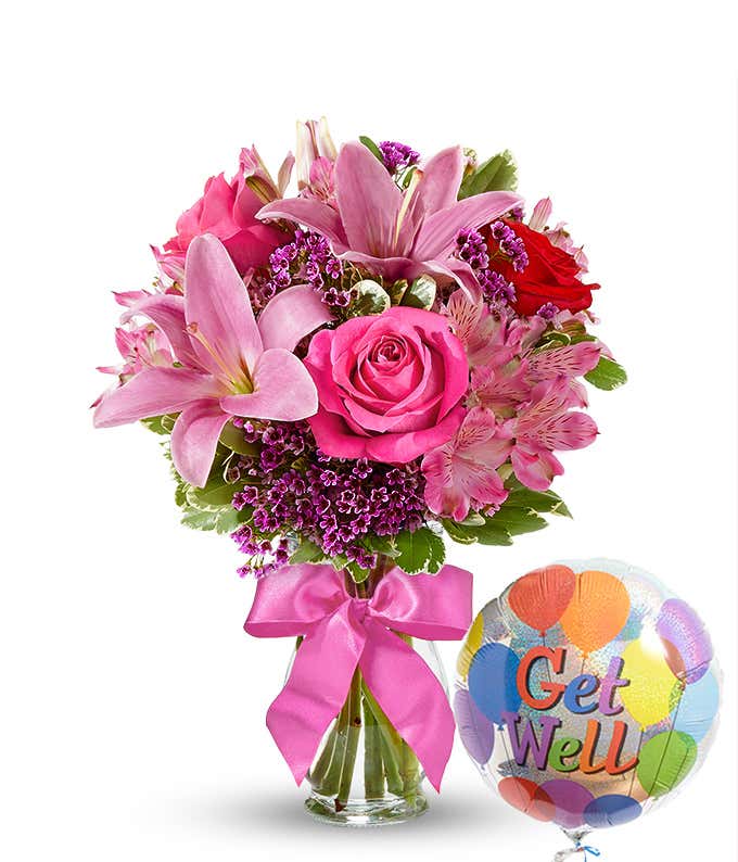 Clear glass vase filled with pink lilies, hot pink roses, red roses, pink alstroemeria, and purple filler flowers, tied with a pink bow and paired with a colorful 'Get Well' balloon. 