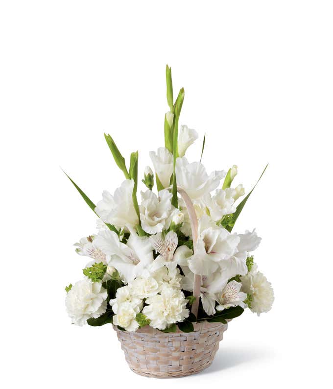 White basket arrangement with white gladiolus, white carnations, white alstroemeria, and greenery, styled in a fan shape with tall blooms rising in the center.