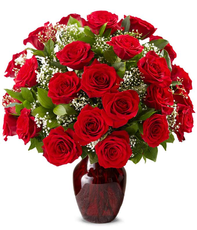 Red rose bouquet with baby's breath and greenery arranged in a deep red glass vase.