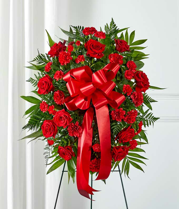A heartfelt standing spray featuring red roses and carnations with floral greens, arranged by your local florist and hand-delivered with a decorative red bow.