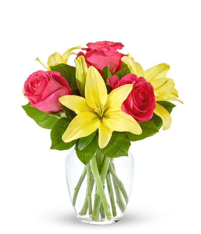 An arrangement featuring yellow lilies and pink roses in a clear glass vase.