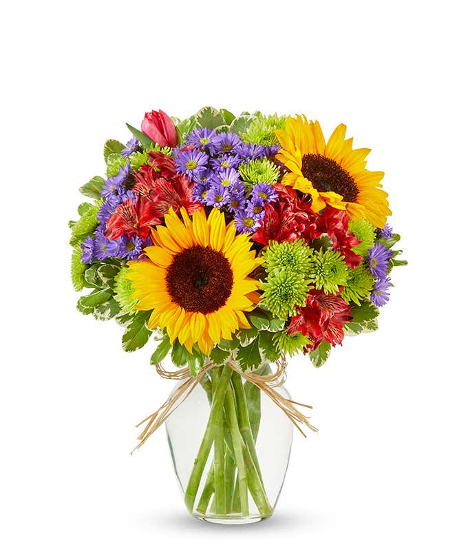Sunflowers and pastel flowers in a clear glass vase with raffia tie