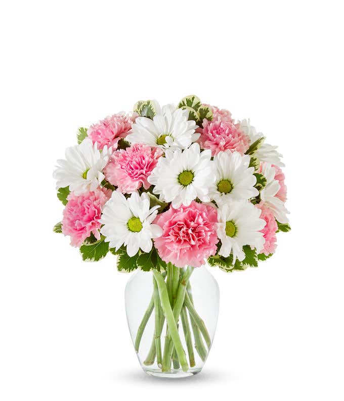 A bouquet of pink roses, pink carnations, and white daisy poms with greenery in a clear glass vase.