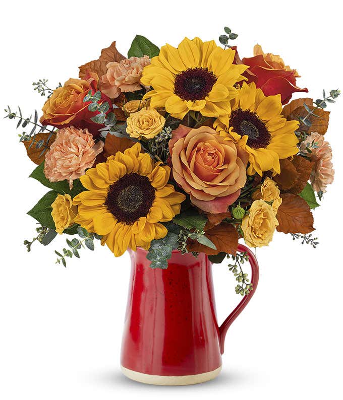 Orange Roses, Yellow Spray Roses, Peach Carnations, Yellow Sunflowers, and Floral Greenery in a Red Ceramic Vase