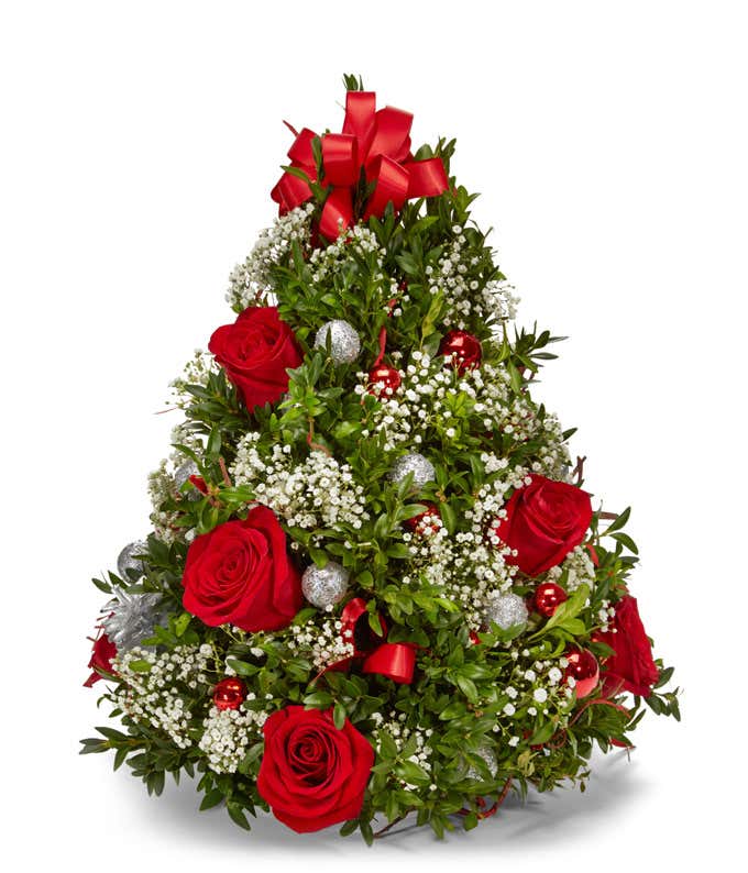 Christmas tree-shaped floral arrangement featuring red roses, baby's breath, lush greenery, silver and red ornament balls, and a large red bow on top.