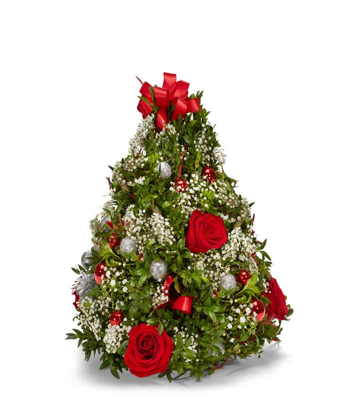 Christmas tree-shaped floral arrangement featuring red roses, baby's breath, lush greenery, silver and red ornament balls, and a large red bow on top.