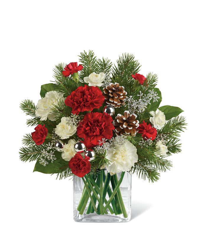 A festive arrangement with red roses (deluxe & premium only), red carnations, white carnations, red mini-carnations, white mini-carnations, seasonal greens, silver ornaments, and pine cones.