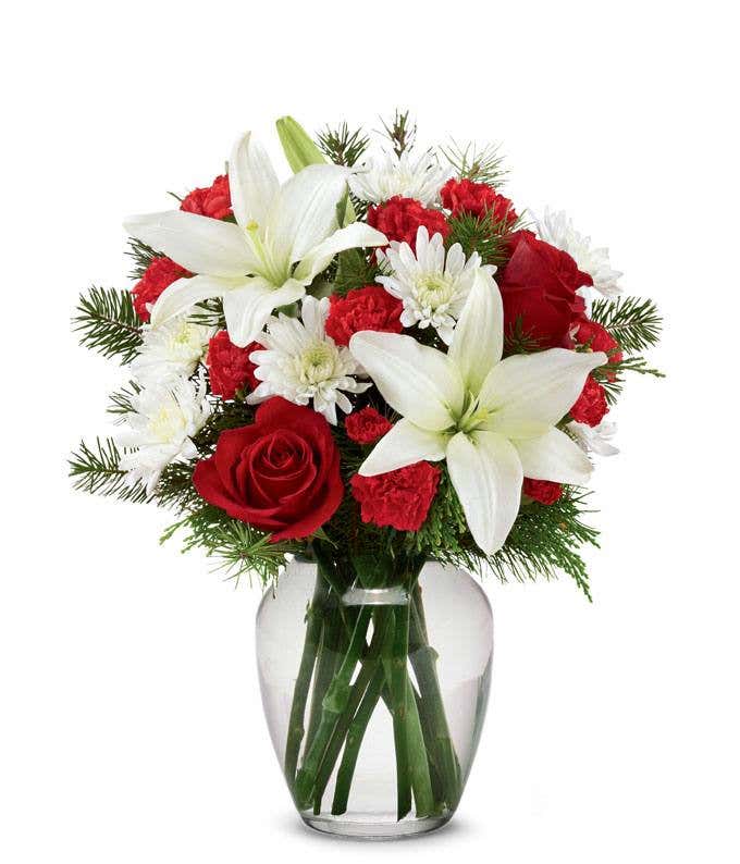 A festive arrangement with red roses, white lilies, red carnations, red mini carnations, and white poms.