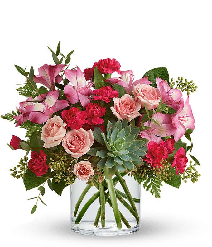 A vibrant floral arrangement featuring pink mini roses, pink alstroemeria, pink mini carnations, a succulent plant, and hot pink roses in deluxe and premium versions.