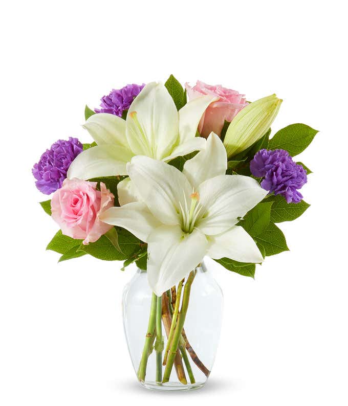 pink roses, purple carnations and white lilies in a clear Vase
