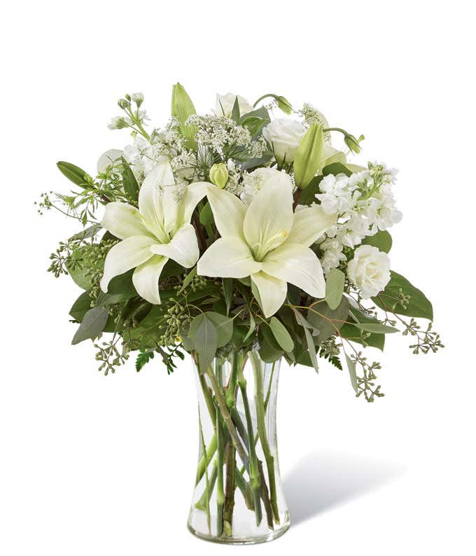 An elegant arrangement featuring white lilies, white lisianthus, white stock, Queen Anne's lace, white veronica, and eucalyptus, beautifully presented in a tall clear cylinder vase. Includes a complimentary card message for a personal touch.