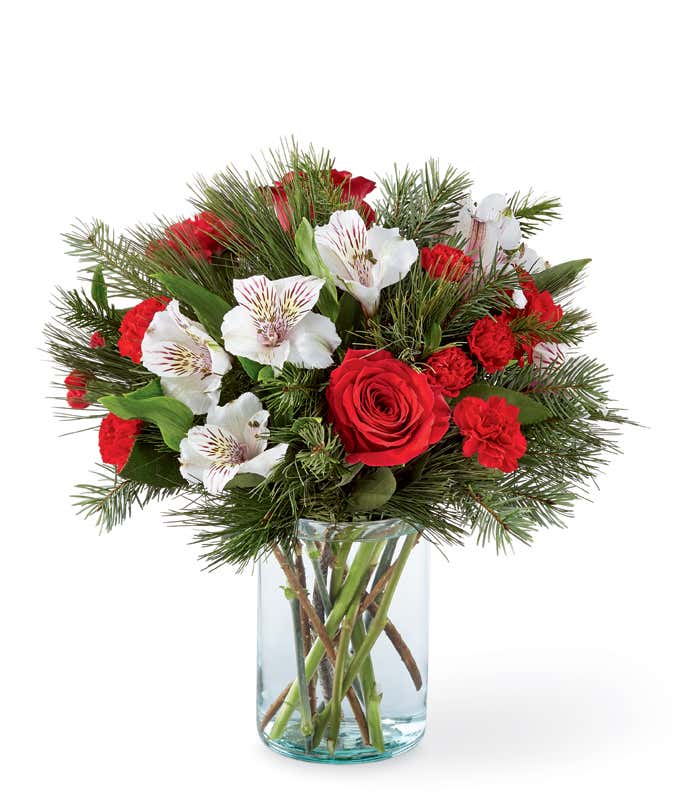 Festive bouquet featuring red roses, white alstroemeria, red carnations, and pine greenery arranged in a clear glass vase for a classic holiday look. A lush and elegant floral display that brings Christmas warmth and beauty to any setting.