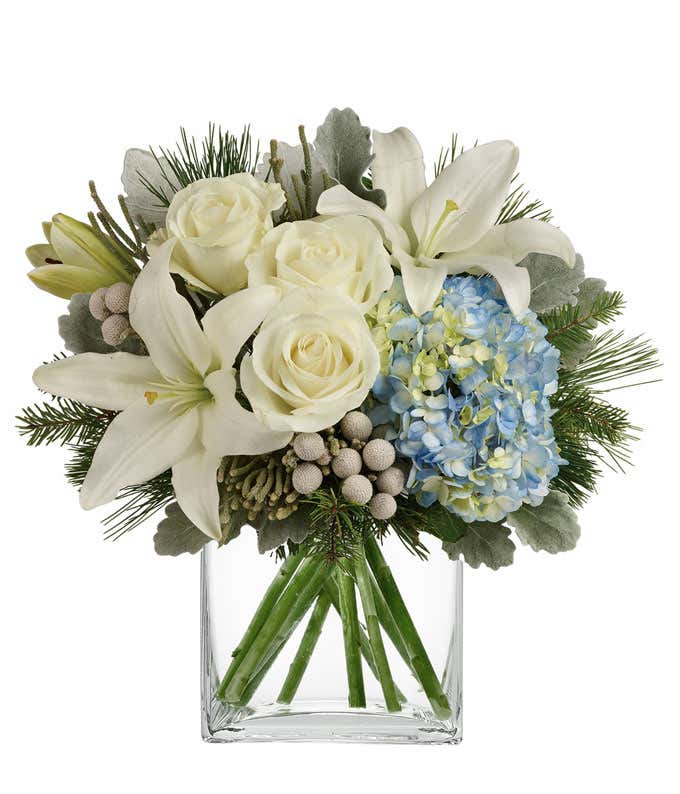 A bouquet of blue hydrangea with white lilies, roses, and berries. Filled out with evergreens and dusty miller.