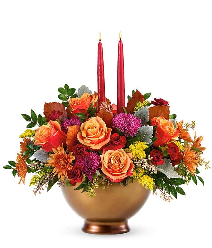 Centerpiece featuring orange roses, maroon miniature carnations, rust and purple cushion spray chrysanthemums, solidago, brown copper beech, dusty miller, seeded eucalyptus, and huckleberry, complemented by burgundy candle.