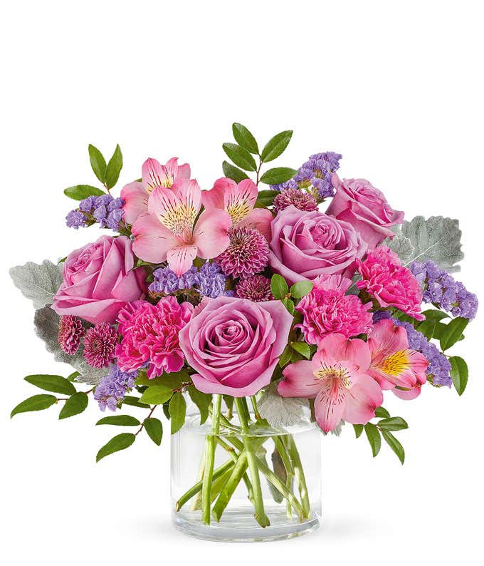 Lavender Roses, Pink Alstroemeria, Fuchsia Carnations, Purple Button Poms, and Floral Greenery in a Short Clear Cylinder Vase