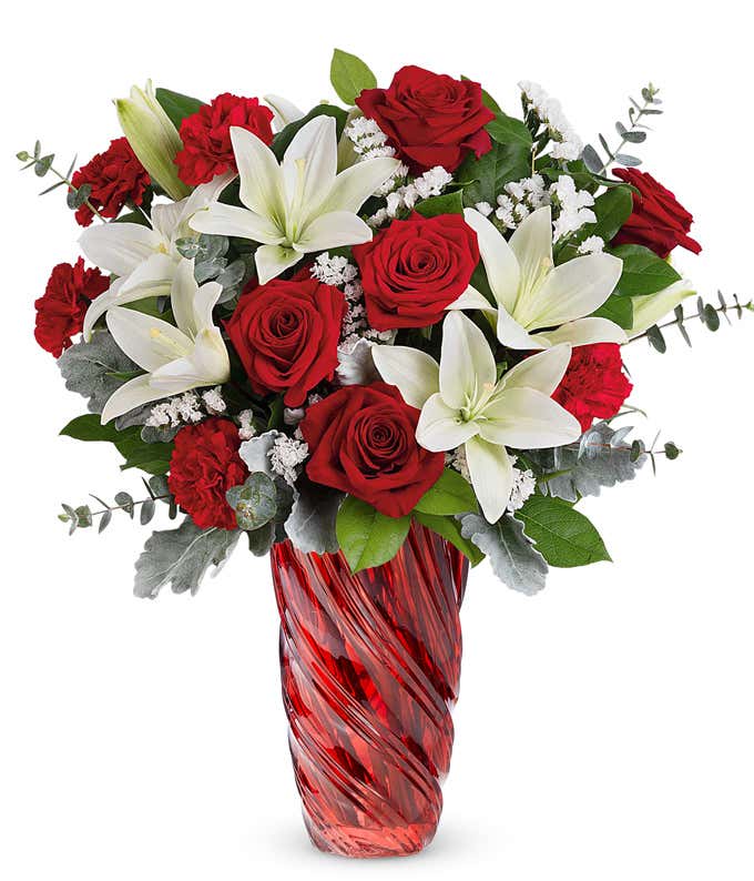 A tall and large bouquet of red roses, white lilies, and soft silver greenery in a tall red swirled vase