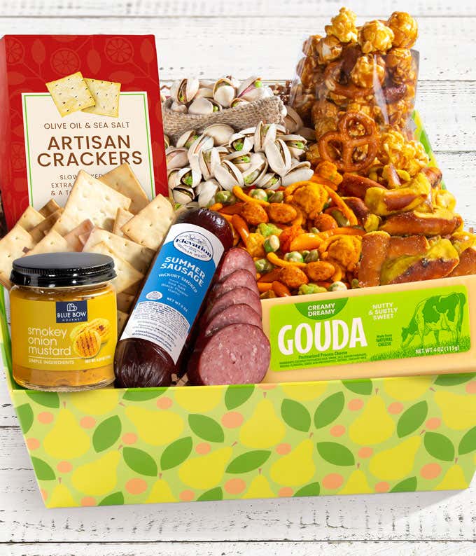 The image features a snack box filled with artisan crackers, gouda cheese, sausage, and mustard, along with pretzels and other snacks. The items are neatly packed in a colorful box with a bright, cheerful design. 