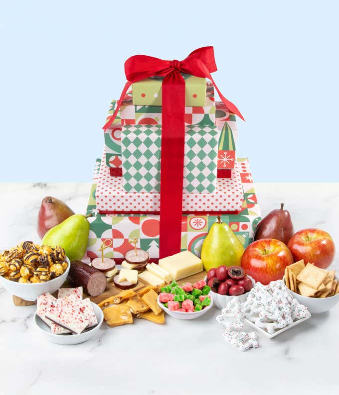 A festive holiday-themed gift tower adorned with a large red bow. Inside the tower are fresh pears, apples, blocks of cheese, crackers, peppermint bark, popcorn, and assorted holiday treats. 