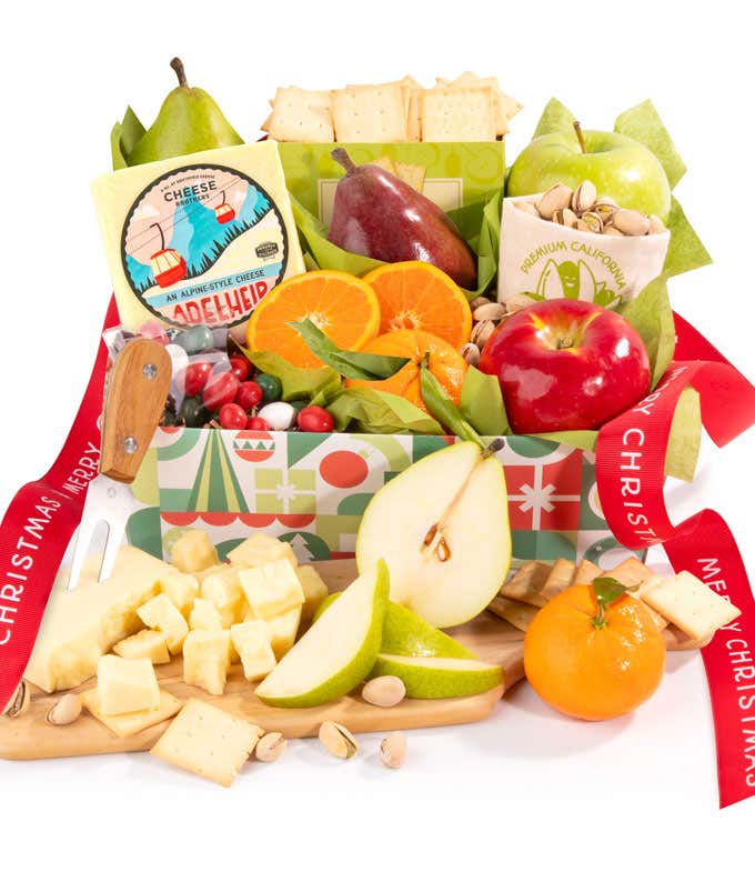 A holiday gift box filled with fresh apples, pears, oranges, crackers, cheese, pistachios, and festive holiday candies, all arranged with green tissue paper for a festive presentation. 