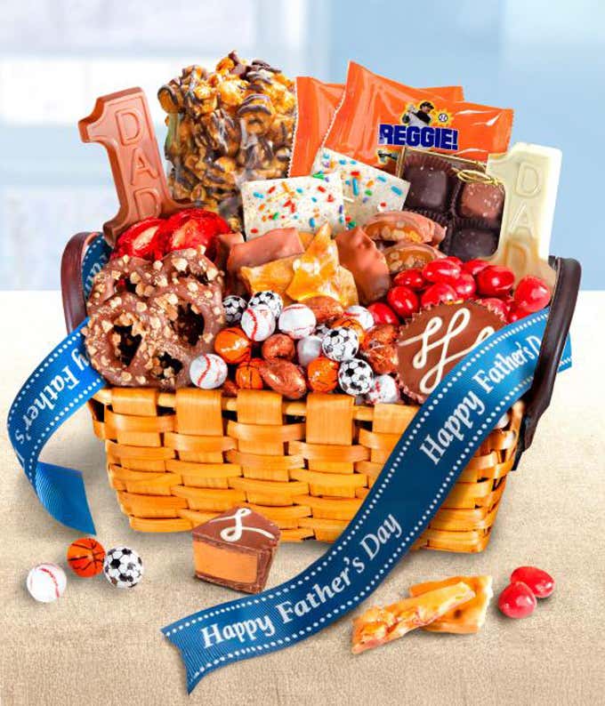 Fathers Day candy gift basket filled with assorted sweets including chocolate-covered pretzels, caramel popcorn, chocolate bars, brittle, colorful candy pieces, and novelty sports-themed chocolates, decorated with a blue Happy Fathers Day ribbon.