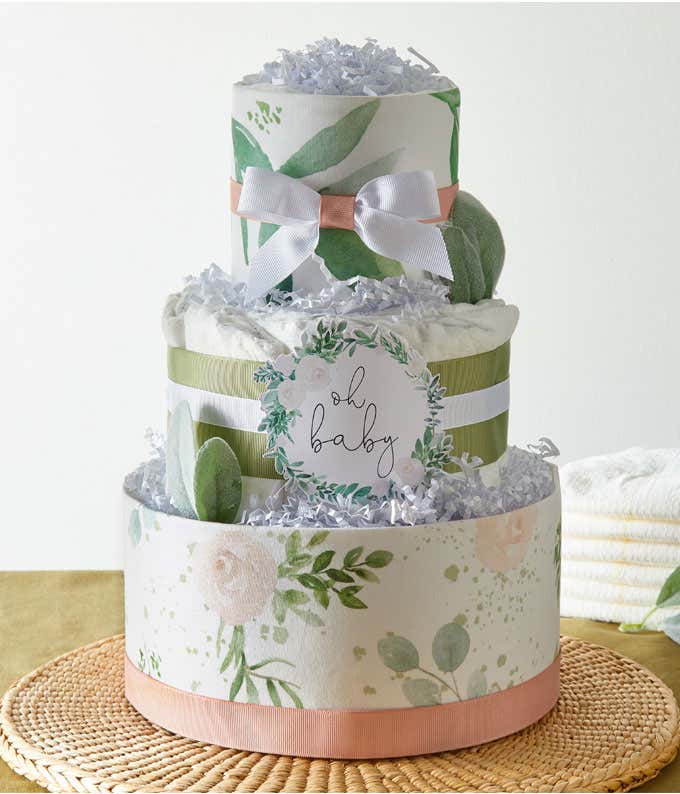 A three-tier diaper cake with green and pink floral patterns, topped with a white ribbon and 'Oh Baby' sign, surrounded by decorative shredded paper.