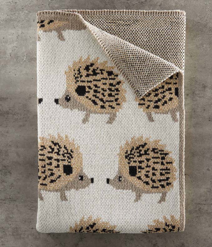 A folded blanket featuring a pattern of hedgehogs, with brown and black details, on a grey background.