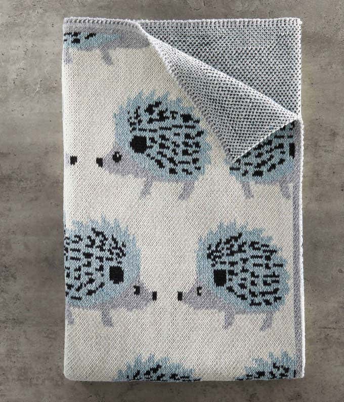 A folded blanket featuring a pattern of blue hedgehogs on a grey background. 