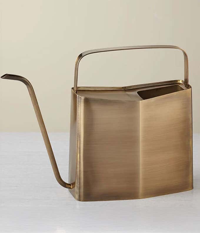 Modern brass watering can with a sleek, angular design featuring a long, curved spout and a wide, geometric handle.