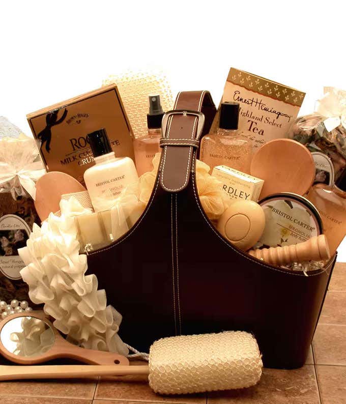 Luxury spa gift basket with bath products, gourmet tea, chocolates, a loofah, and wooden spa tools.