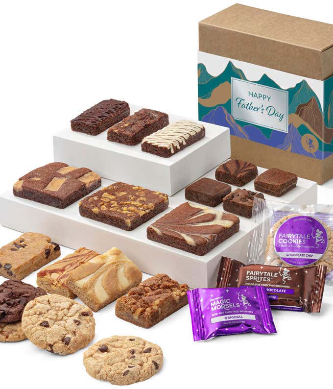 The image displays a box labeled 'Happy Father's Day' with a mountain design, containing assorted brownies and cookies. The treats are arranged on tiered white trays, showcasing various flavors. Fairytale Cookies and Magic Morsels packets are also include