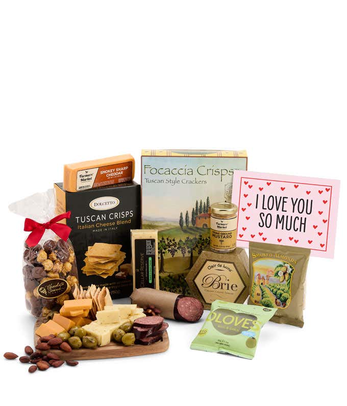 A vibrant gift box featuring 3 cheeses, gourmet crackers, focaccia crisps, summer sausage, olives, smoked almonds, stone-ground mustard, chocolate-covered popcorn, and a pink card with hearts reading 'I Love You So Much.'