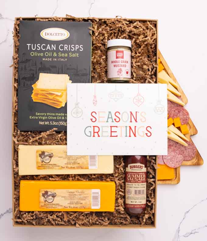 A charcuterie box with two types of cheese, crackers, stone-ground mustard, a summer sausage and a festive message card.