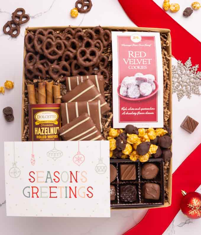 A selection of sweet treats, including a box of assorted chocolates, a box of mini chocolate chip cookies, and a bag of chocolate-covered pretzels accompanied by a Season's Greetings message card for a personal holiday touch.